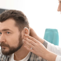 Audiologist inserting a hearing aid in a male patient's ear