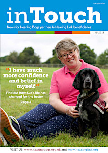 Front cover of inTouch magazone. A smiling woman in a pink shirt is sitting down in a grass field with a black and grey cocker spaniel hearing dog. The dog is wearing a burgundy hearing dogs jacket.