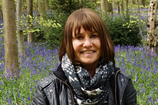 a woman standing among trees with bluebell flowers in the background.