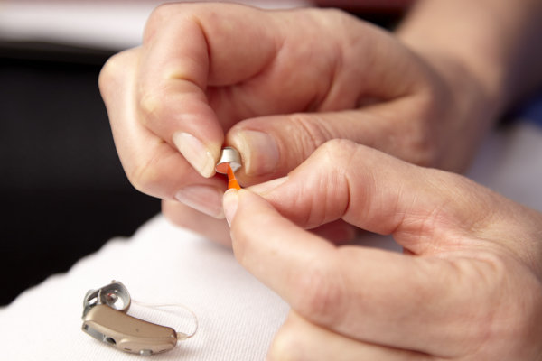 a pair of hands peeling the protective label from a small hearing aid battery